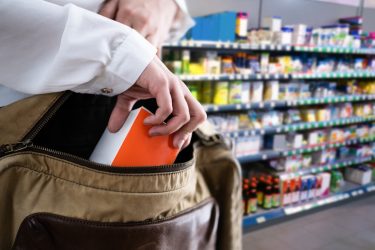 A close up view of a hand covertly pushing a box into an open satchel with pharmacy medications in the background.