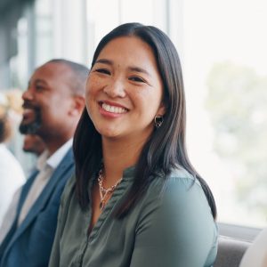 A woman dressed in corporate clothing seated in a row of people smiling and looking at the camera.